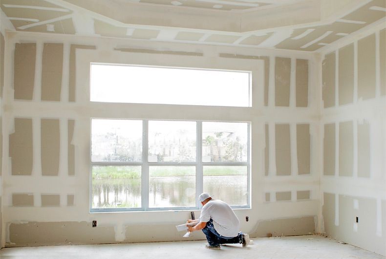 A man is plastering a wall in a room.