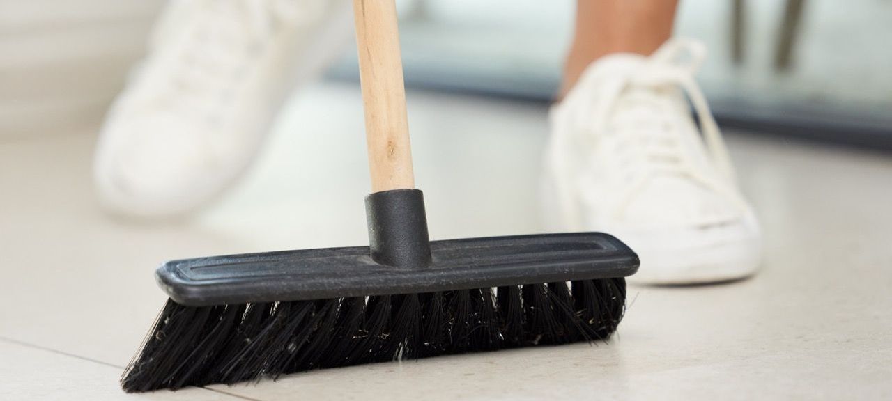 A Person in White Shoes Using a Broom. Ultimate Clean Solutions Will Clean for You in NW Arkansas.