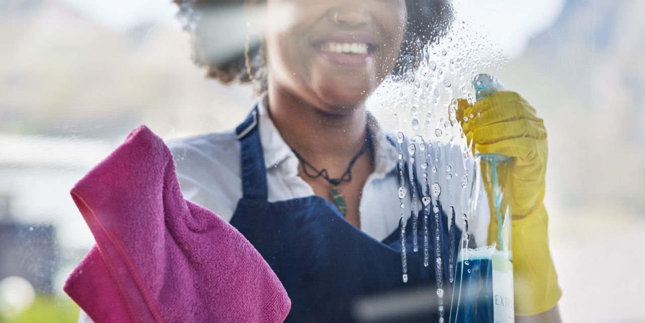 A Woman Washing a Window With a Pink Towel. Ultimate Clean Solutions Is a NWA Cleaning Company.