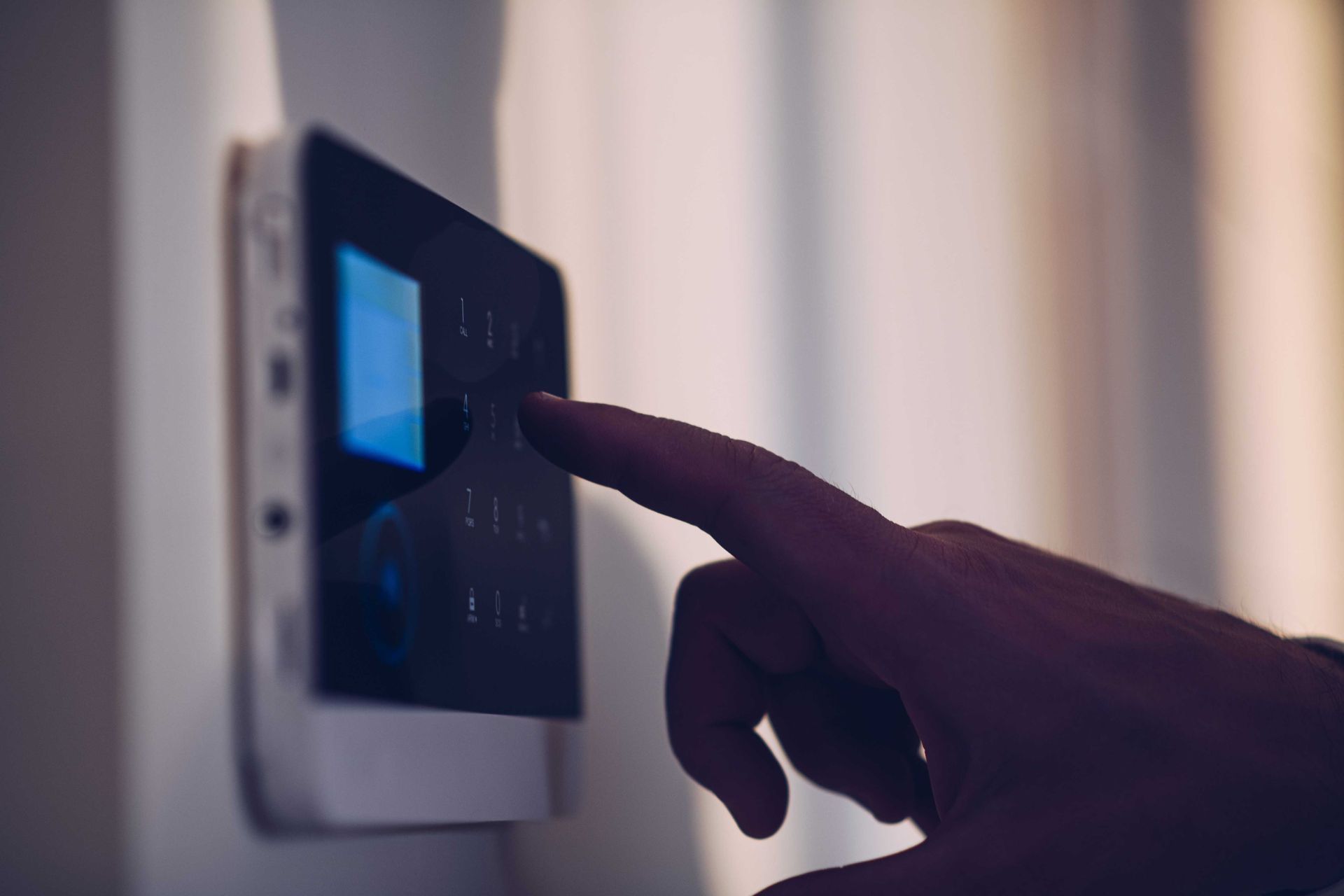 Une main appuie sur un bouton d'un panneau de commande de système de sécurité fixé sur un mur blanc.