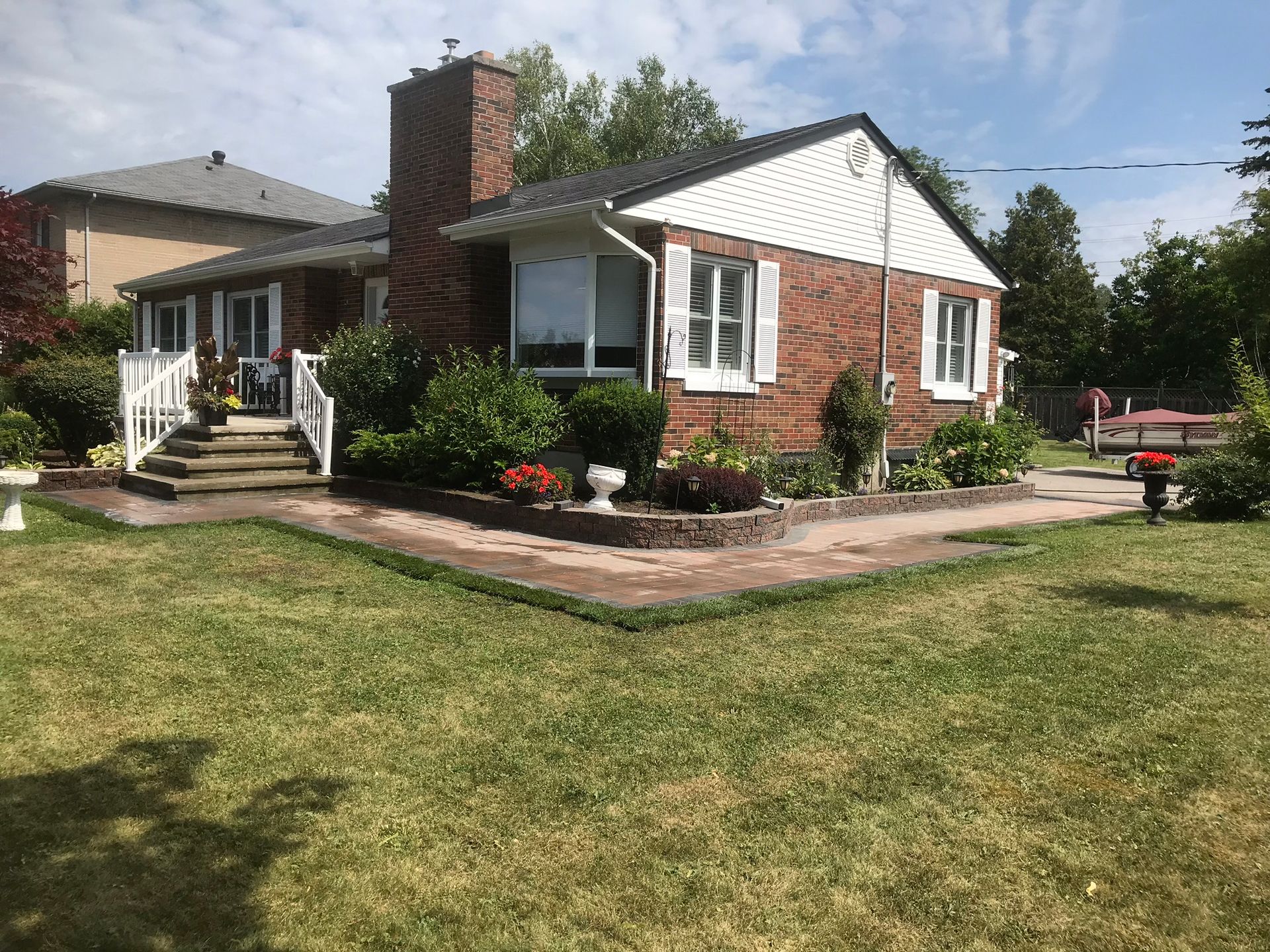 Single-story brick house with white trim, front porch, and landscaped yard under a sunny sky