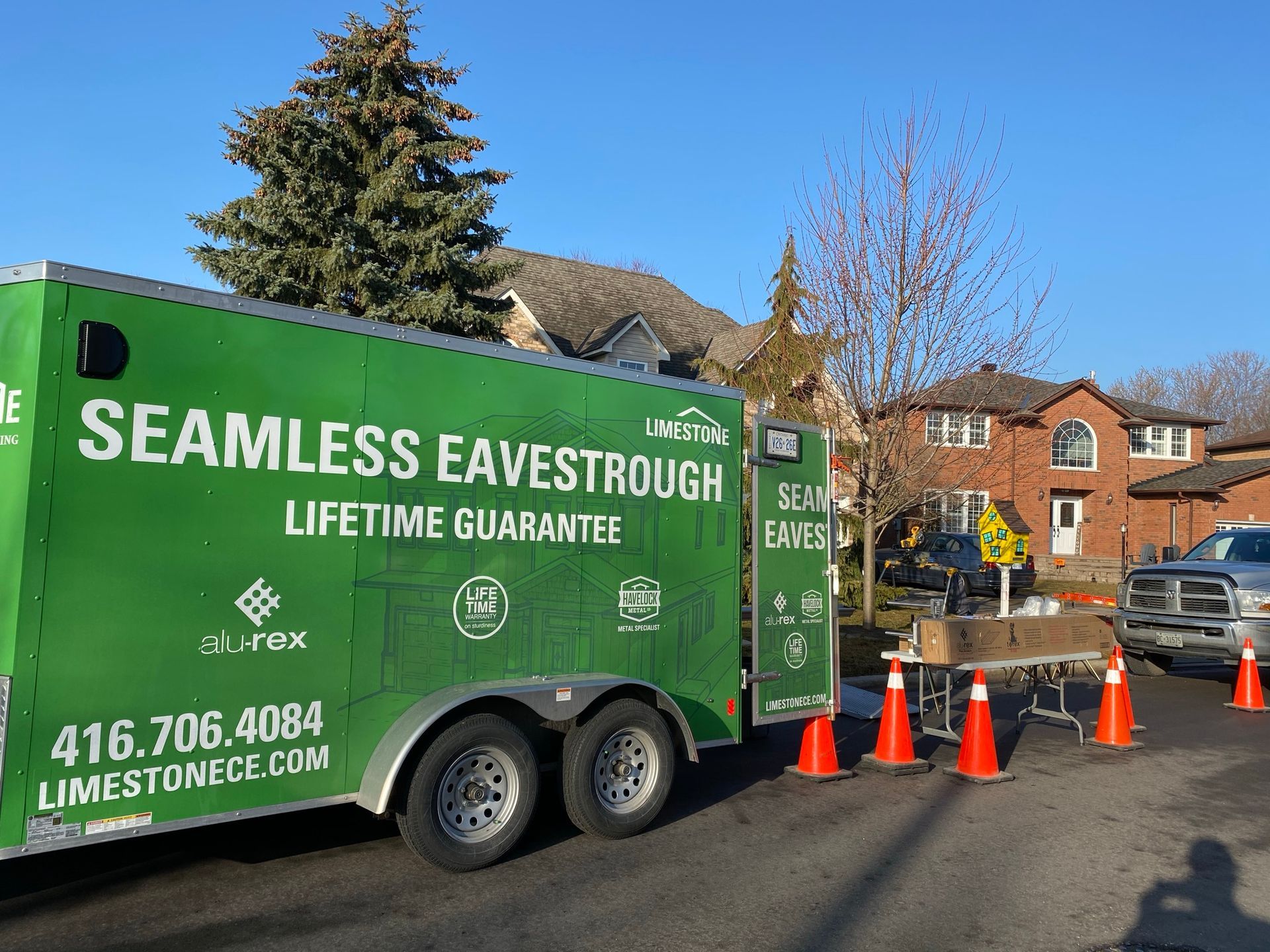 Green Seamless Eavestrough work truck parked by orange cones on a residential street