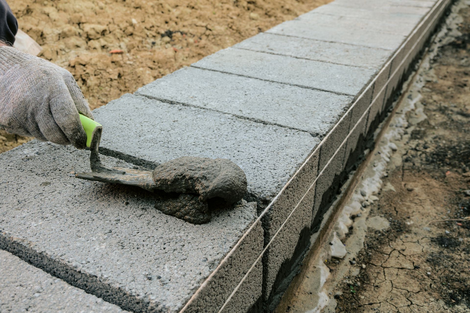 A person is laying bricks on a sidewalk with a trowel.