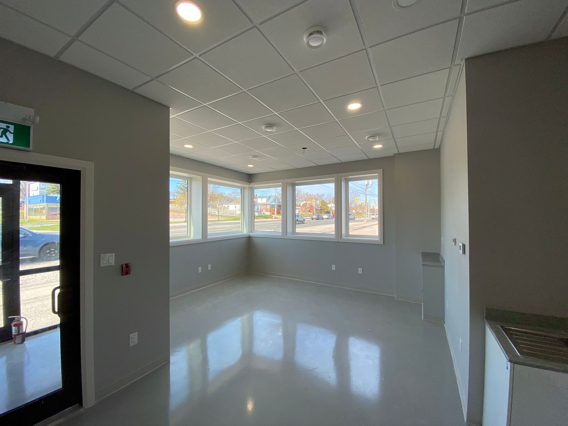 Empty bright office room with white walls, tiled ceiling, large windows, and glossy floor reflections