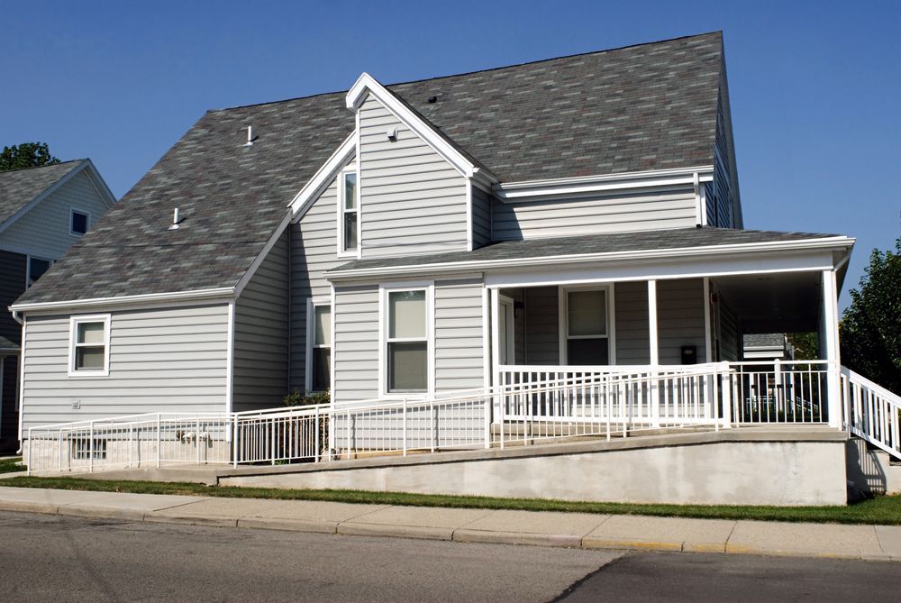 Light gray house with a ramp and screened porch, blue sky.