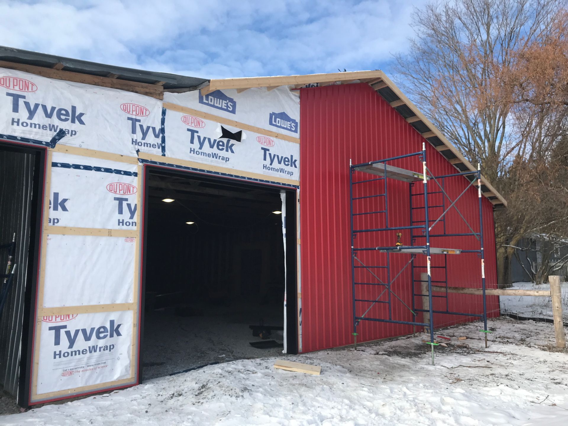 a red barn is being built in the snow with a scaffolding in front of it .