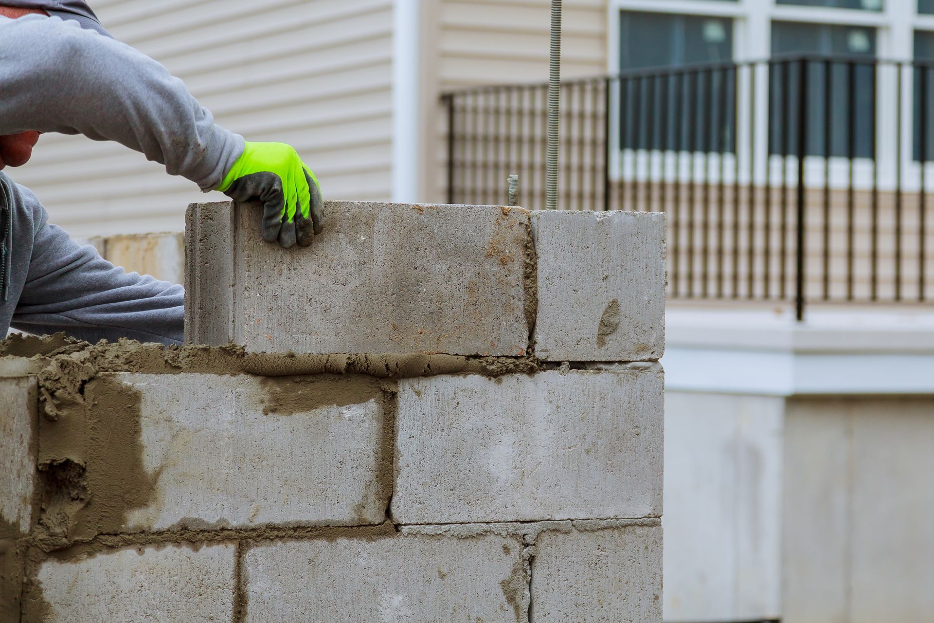 Person in gloves laying concrete blocks, building wall outdoors.