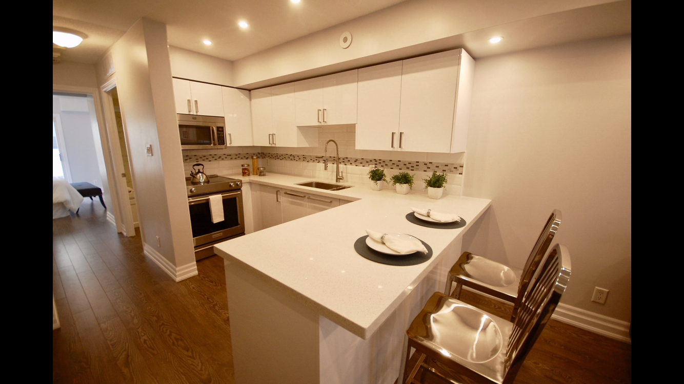a kitchen with white cabinets , a stove , a sink , and a bar .