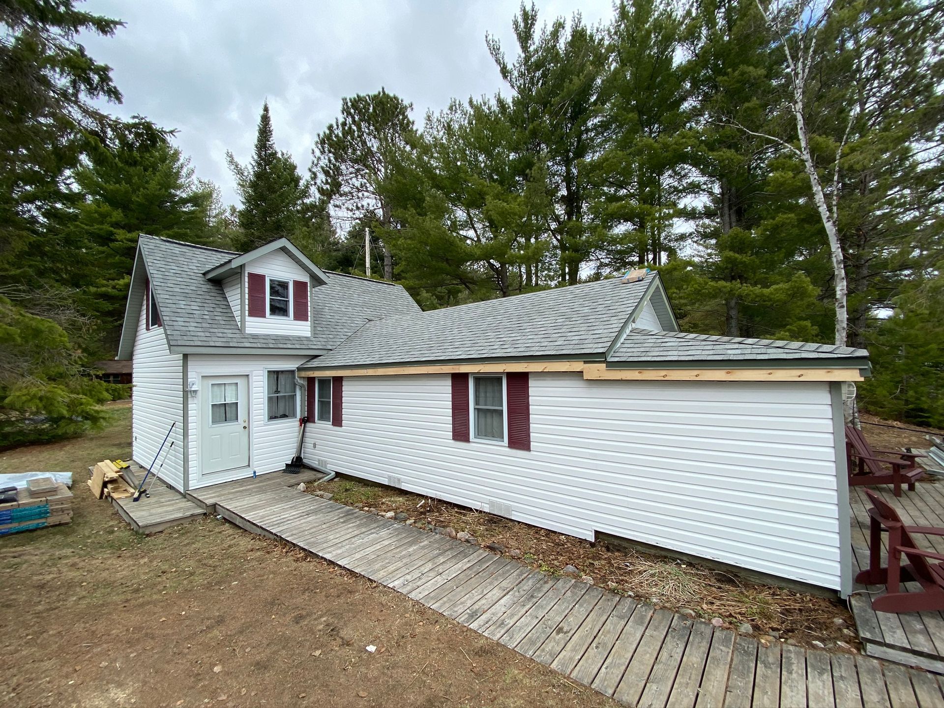 a white house with a gray roof and red shutters is surrounded by trees .