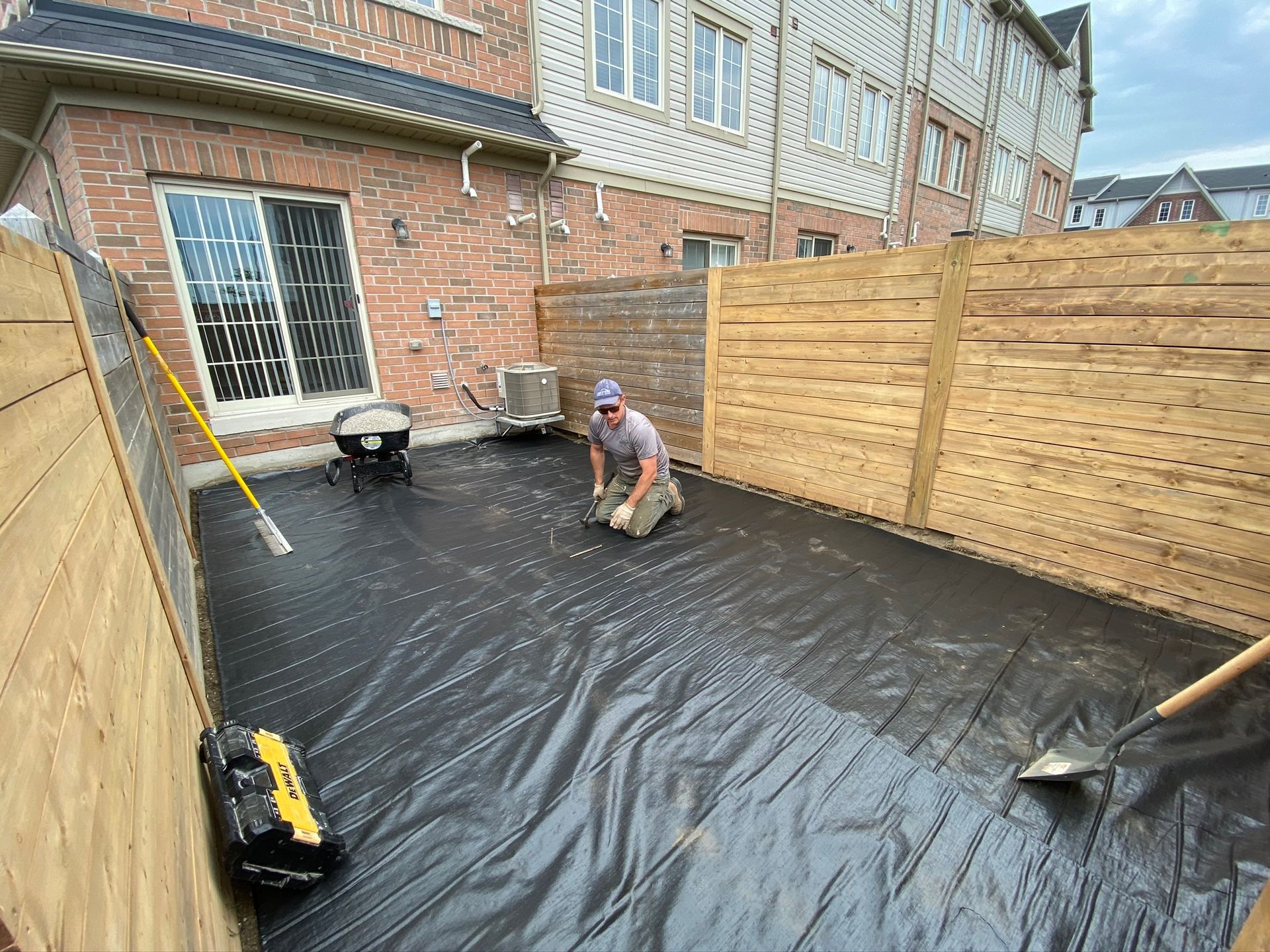 a man is kneeling on a black tarp in a backyard .