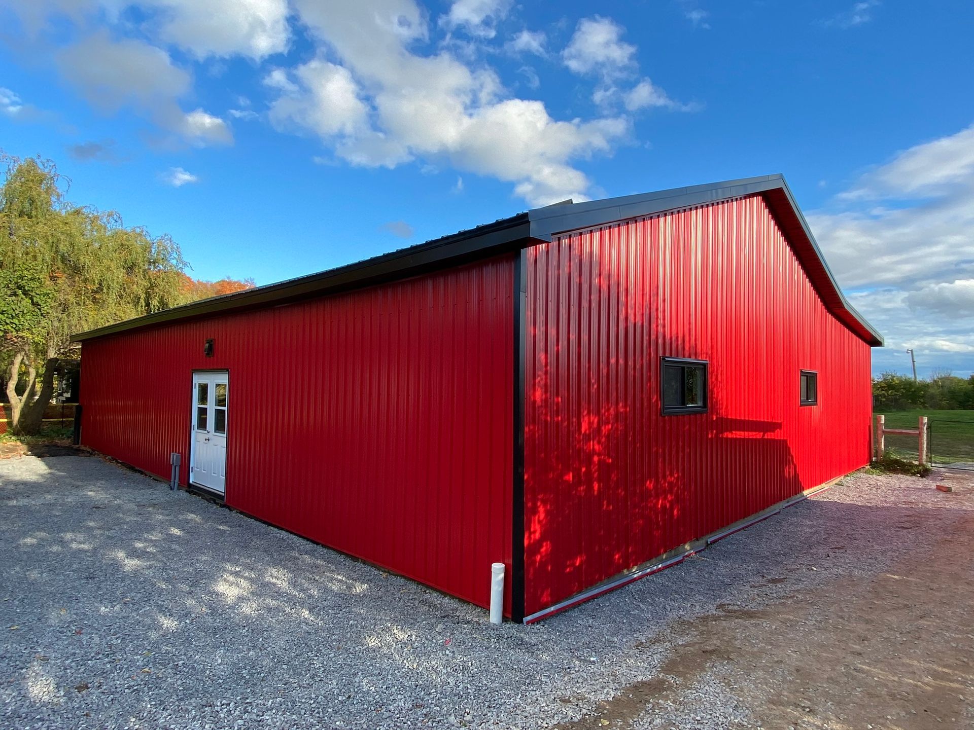 a large red barn with a black roof is sitting on top of a gravel lot