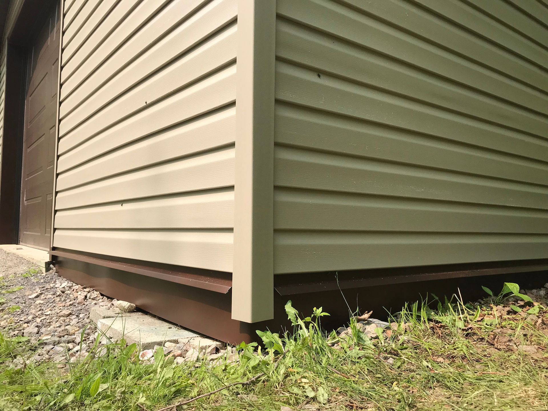 the corner of a house with green siding and a garage door .