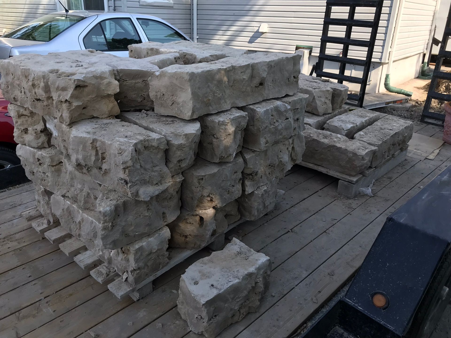 a pile of bricks is sitting on a wooden deck next to a car .