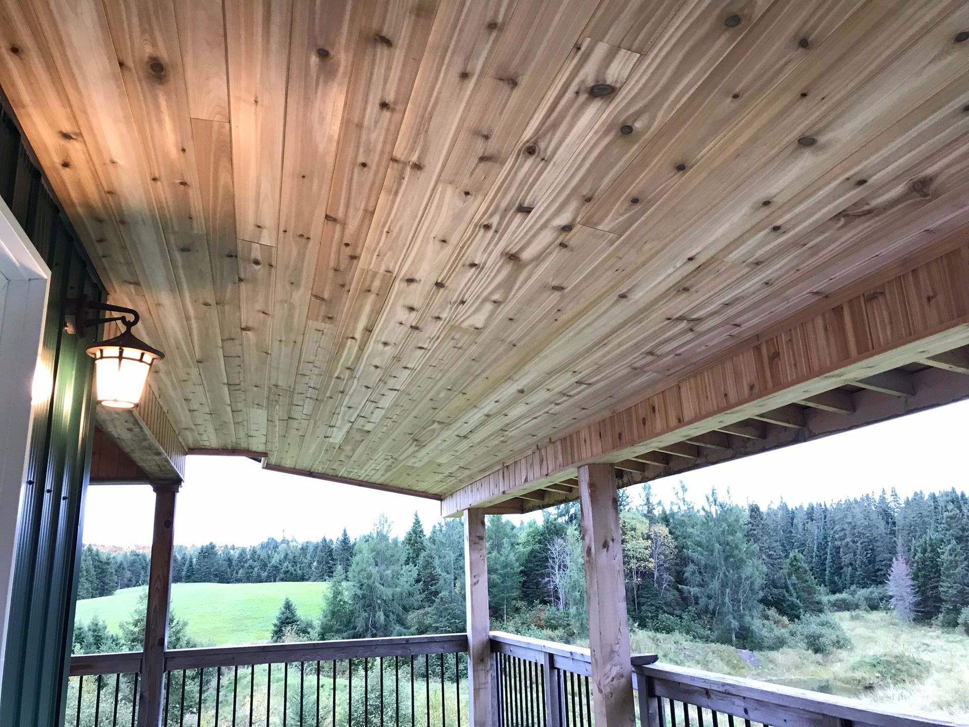a porch with a wooden ceiling and a view of a forest .