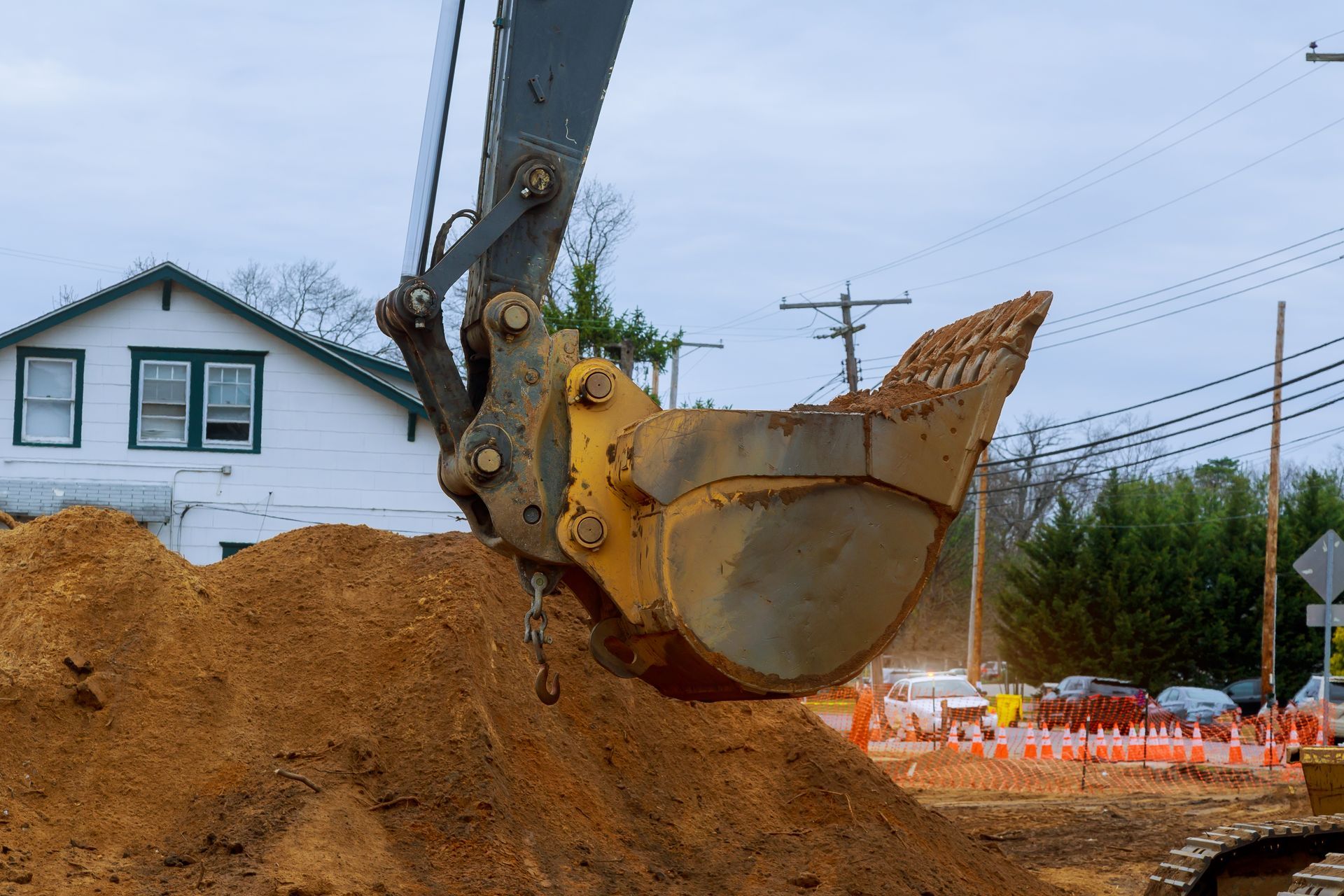 Excavator bucket scooping up dirt next to a house under construction.