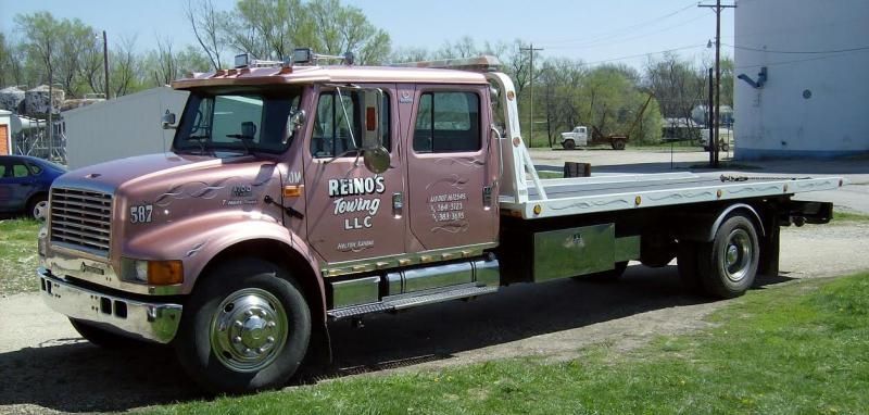 Pink tow truck with a flatbed in a grassy area.