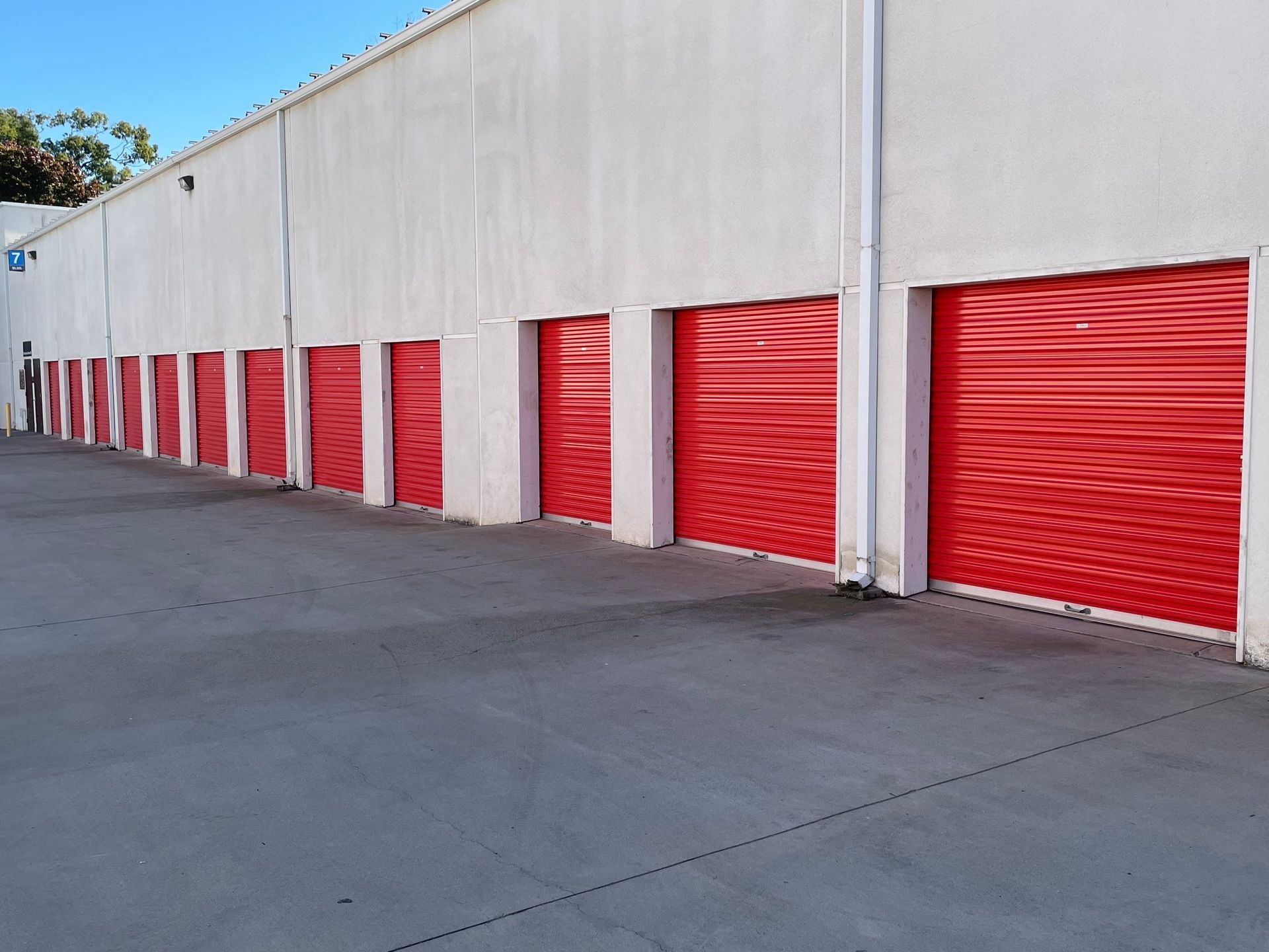 Row of red storage unit doors on a white building, set on a concrete lot.