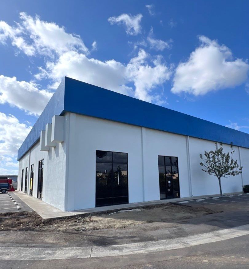 White commercial building with blue roof, black windows, and a tree, under a cloudy sky.