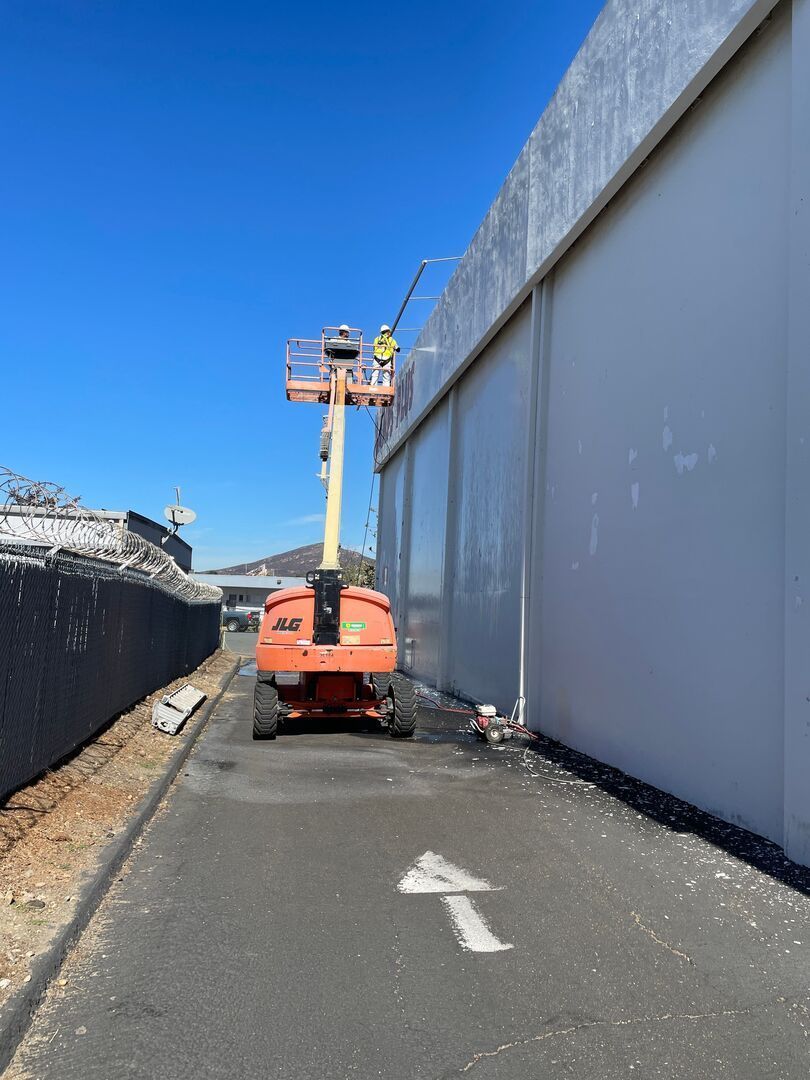 Orange lift platform near a large, light-colored wall.  An arrow points to the left on the asphalt.