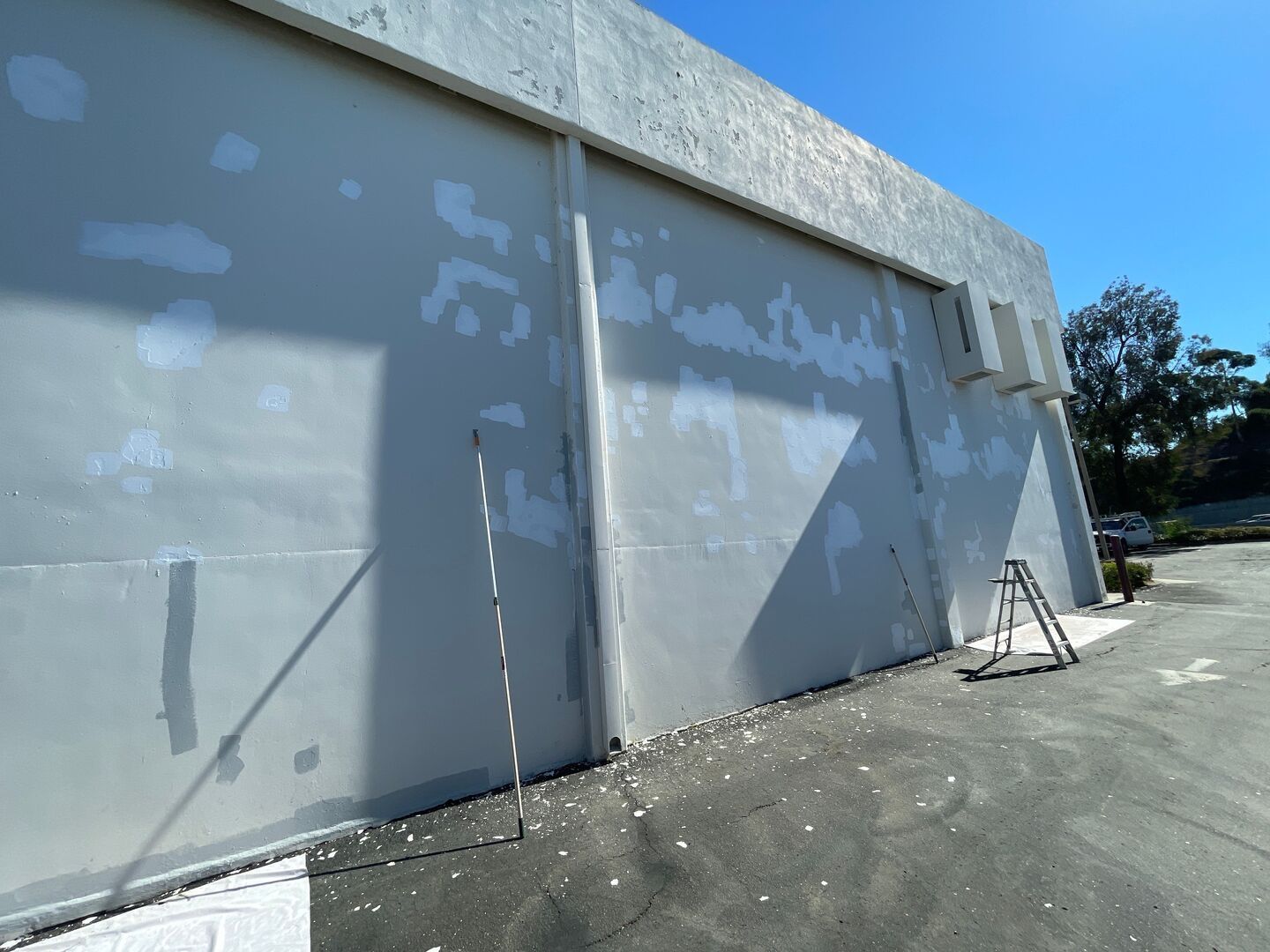 Exterior building wall with repair patches, ladder, bright blue sky.
