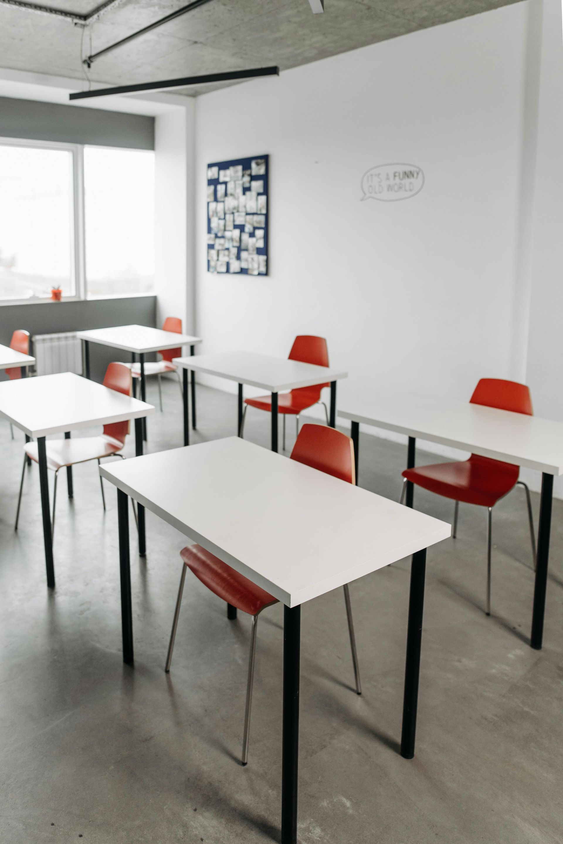 An empty classroom featuring white desks and orange chairs arranged on a gray floor.