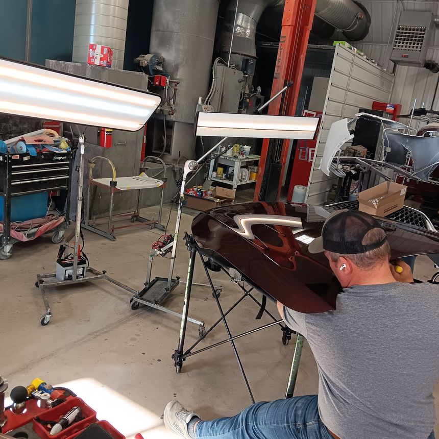 Person polishing a maroon car body in a garage with work lights and tools