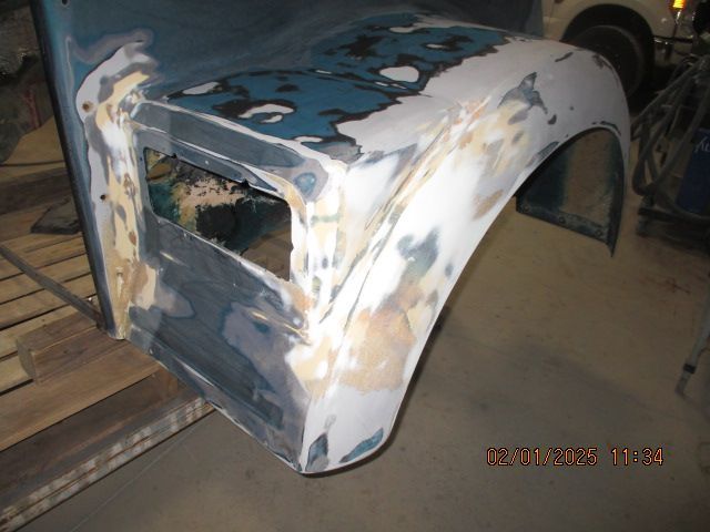 Partially restored vintage car body in primer and bare metal, viewed from the rear side in a workshop