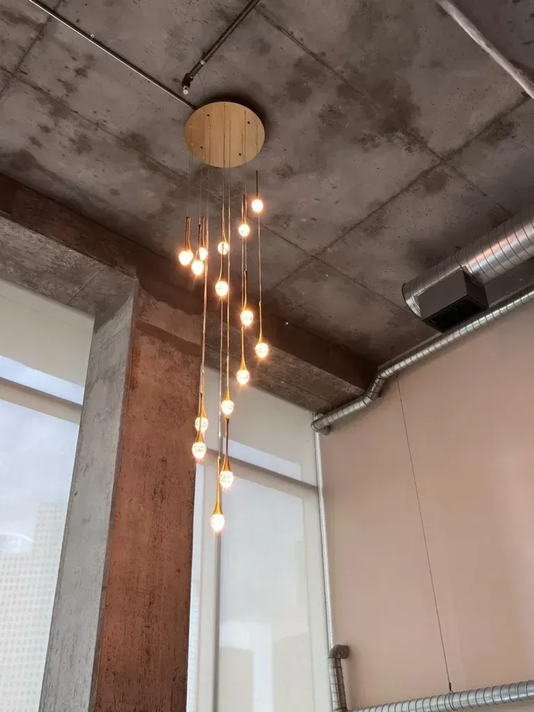 Gold chandelier with spherical bulbs suspended from a circular ceiling mount, in a room with concrete and tan walls.