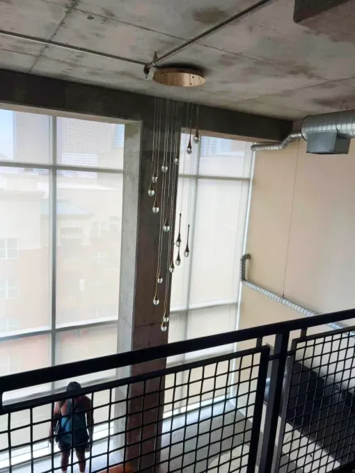 Loft interior with modern light fixture hanging from a concrete beam, overlooking a large window.