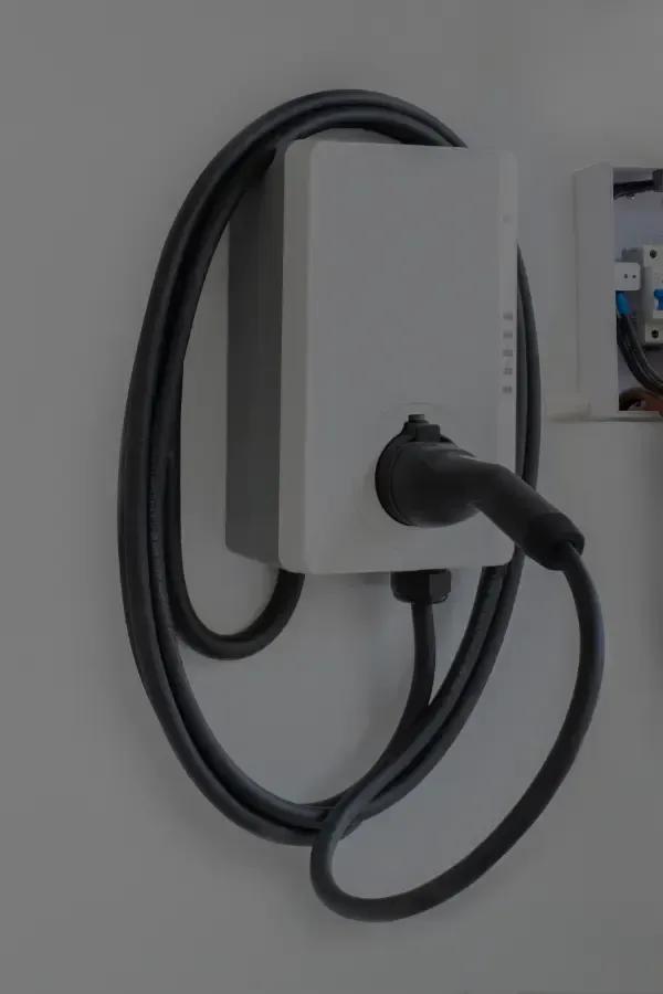 An electric vehicle charger mounted on a white wall with the charging cable coiled around it.