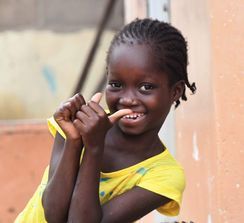 Smiling child in yellow shirt holding a tooth or lollipop near a peach-colored wall