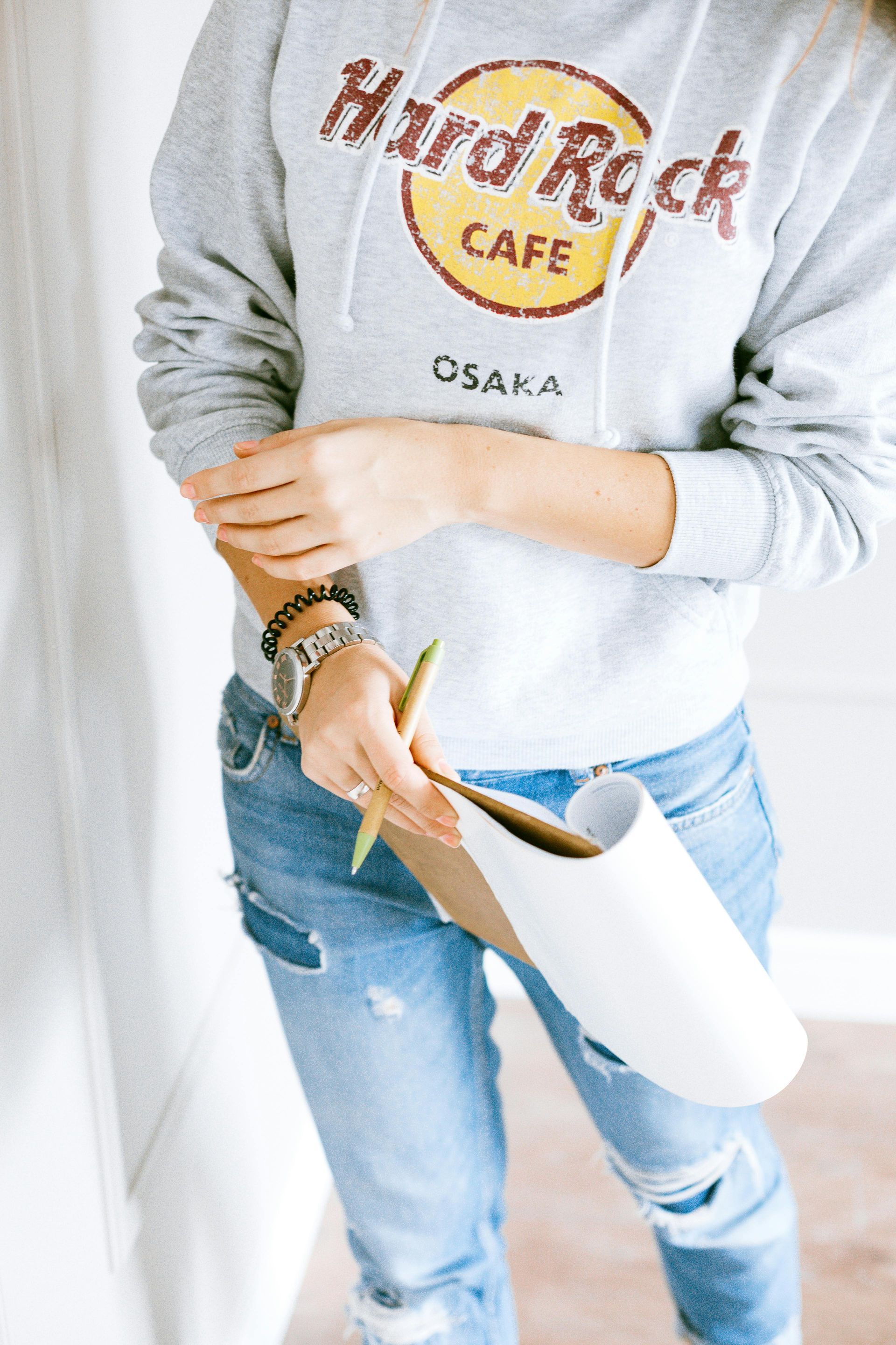 A woman wearing a hard rock cafe hoodie is writing on a clipboard