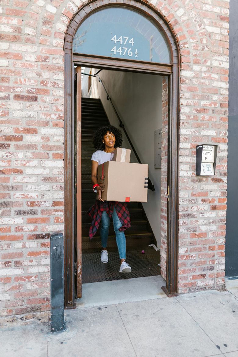 A woman is carrying a cardboard box through a doorway.