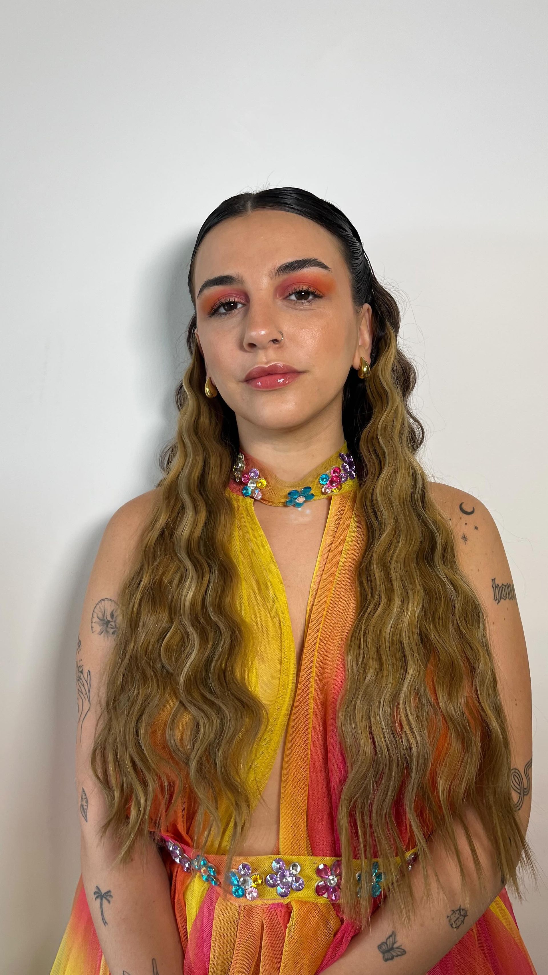 Persona de pie sobre un fondo blanco liso, vestida con un conjunto 