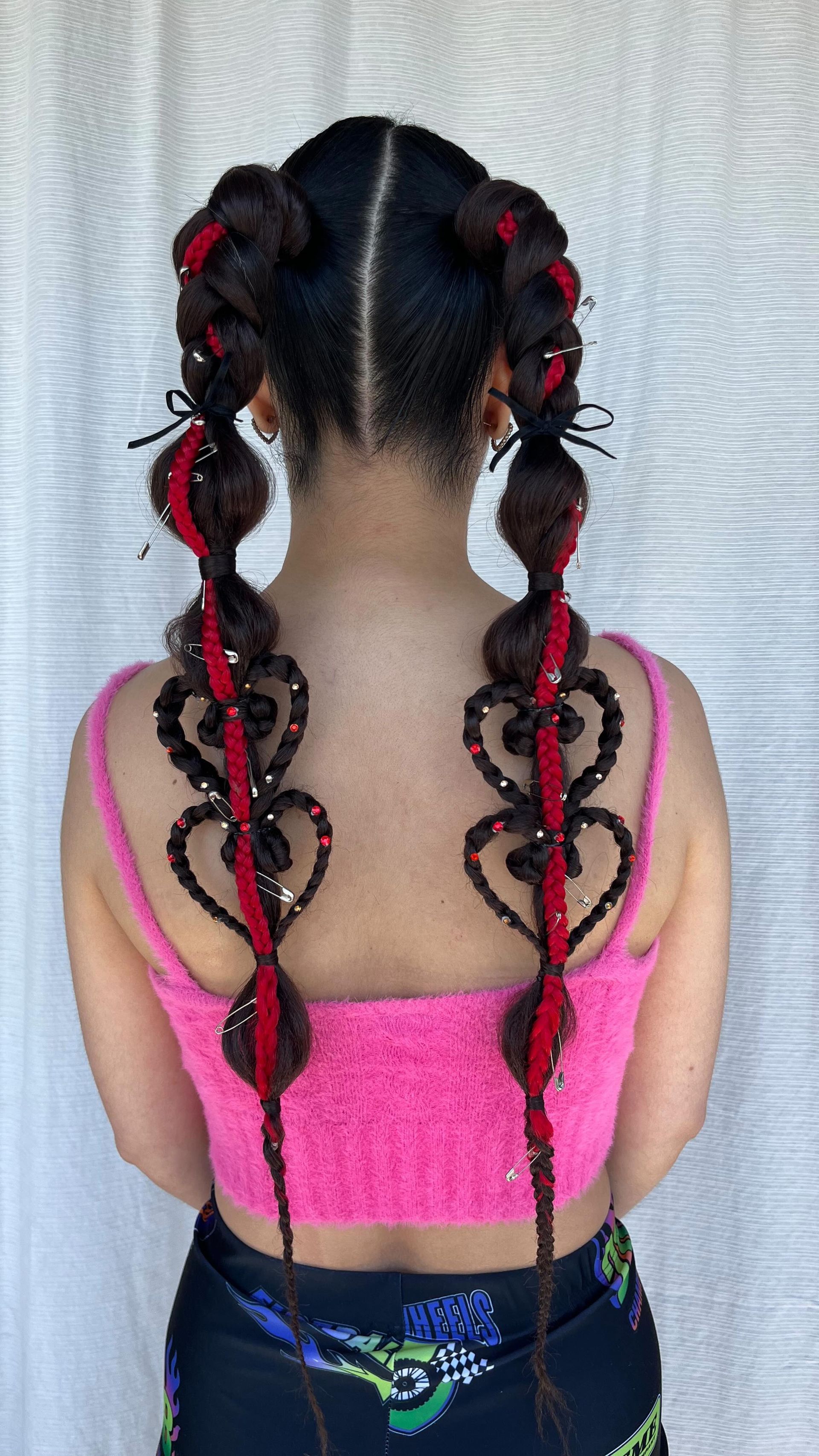 Vista trasera de dos niñas con trenzas y lazos rojos, que visten blusas rosas, frente a una cortina blanca.