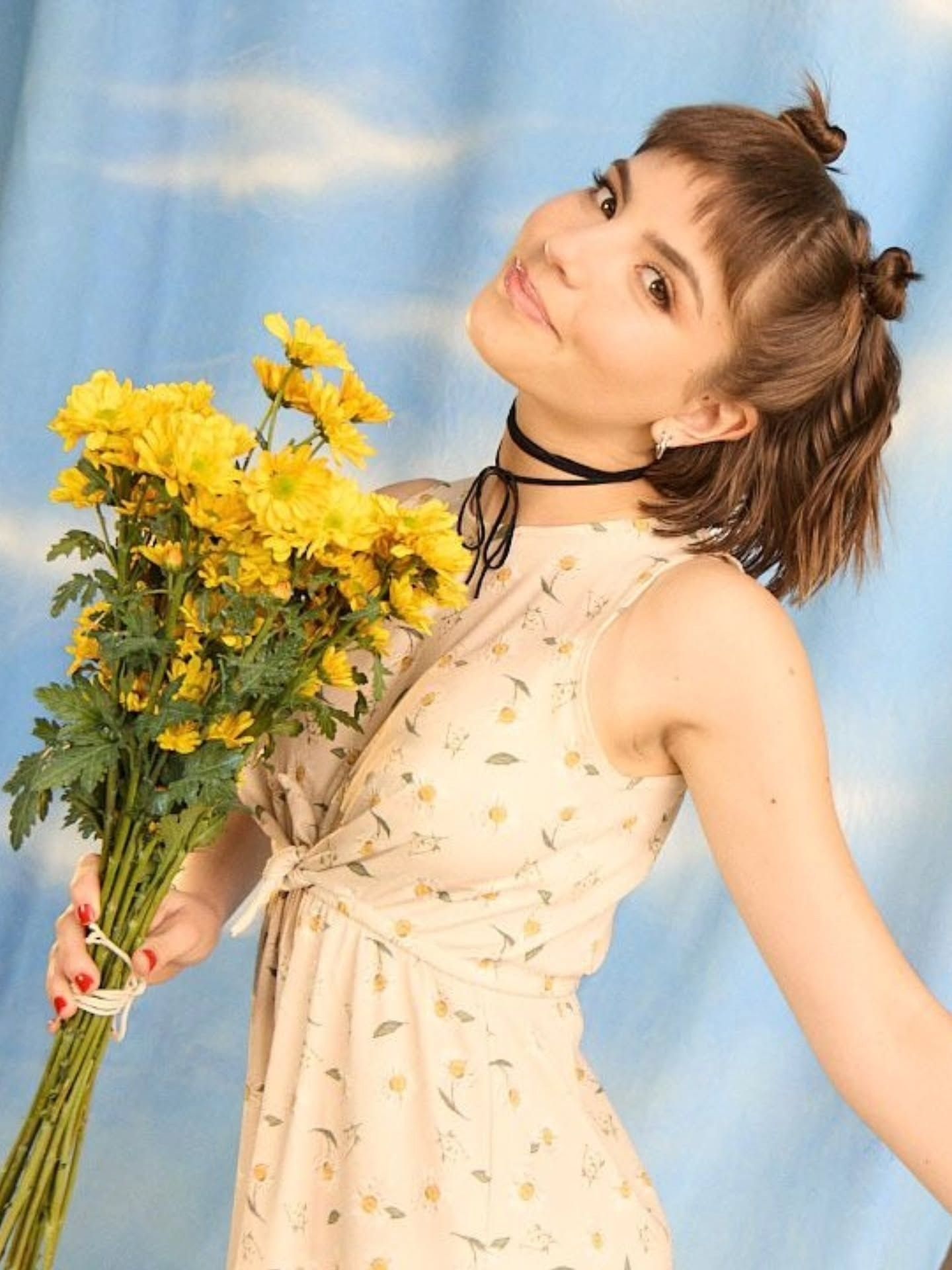 Mujer sosteniendo un ramo de flores amarillas sobre un fondo azul.