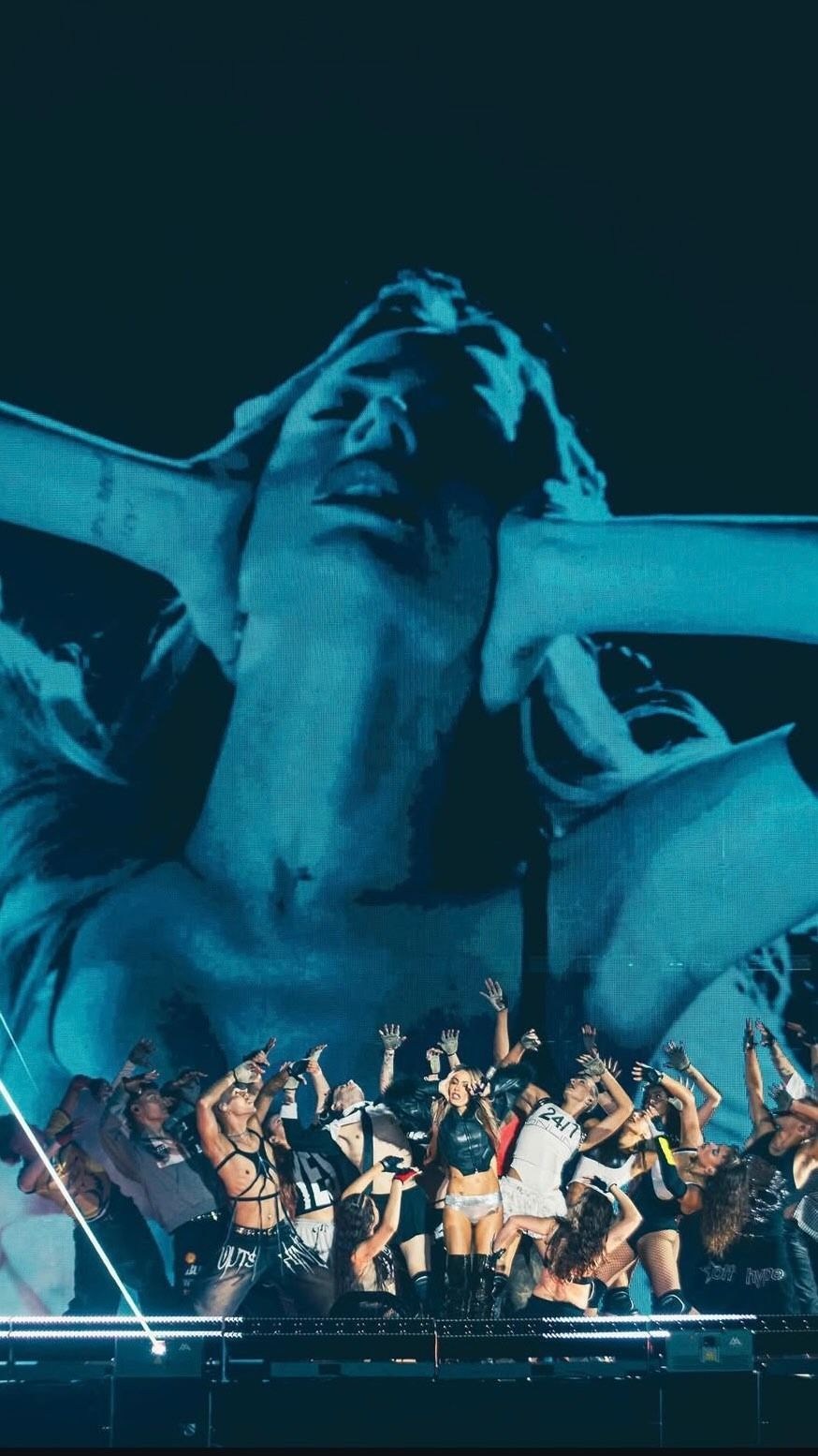 Multitud bailando bajo una estatua gigante iluminada de azul en un escenario de conciertos.