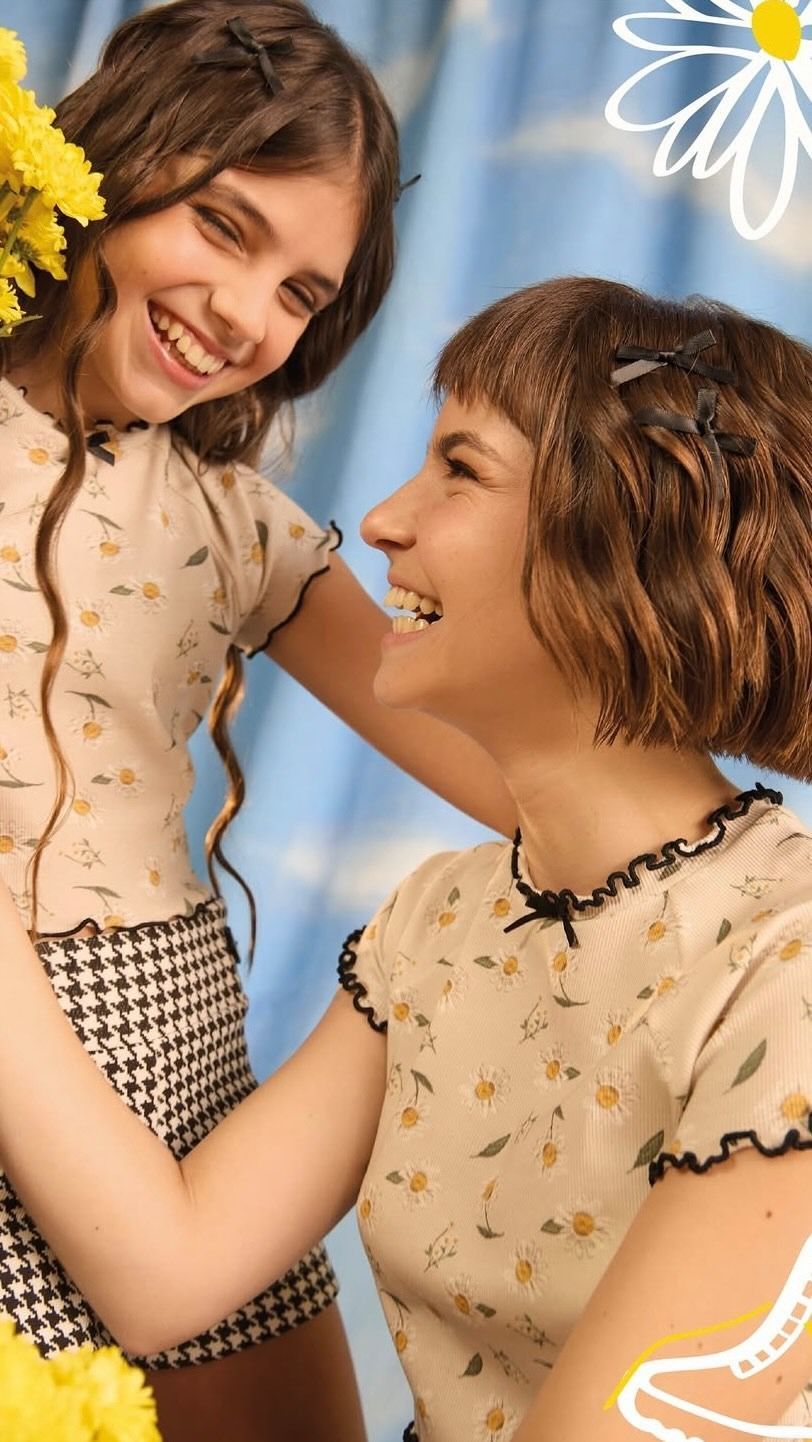 Dos mujeres sonrientes con vestidos beige riendo juntas con un cielo azul de fondo.