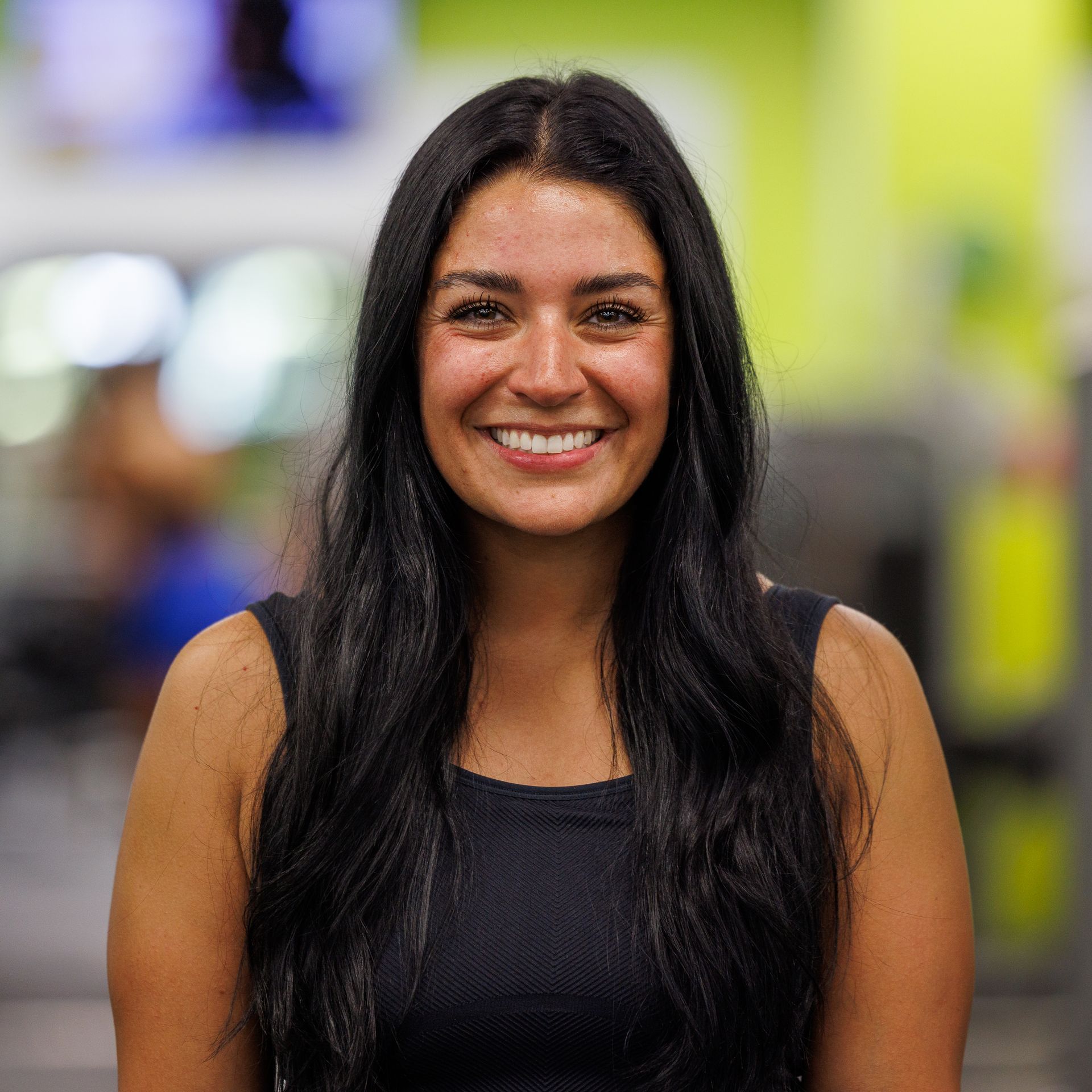 Woman with dark hair smiling at the camera in a gym setting, wearing a black top.