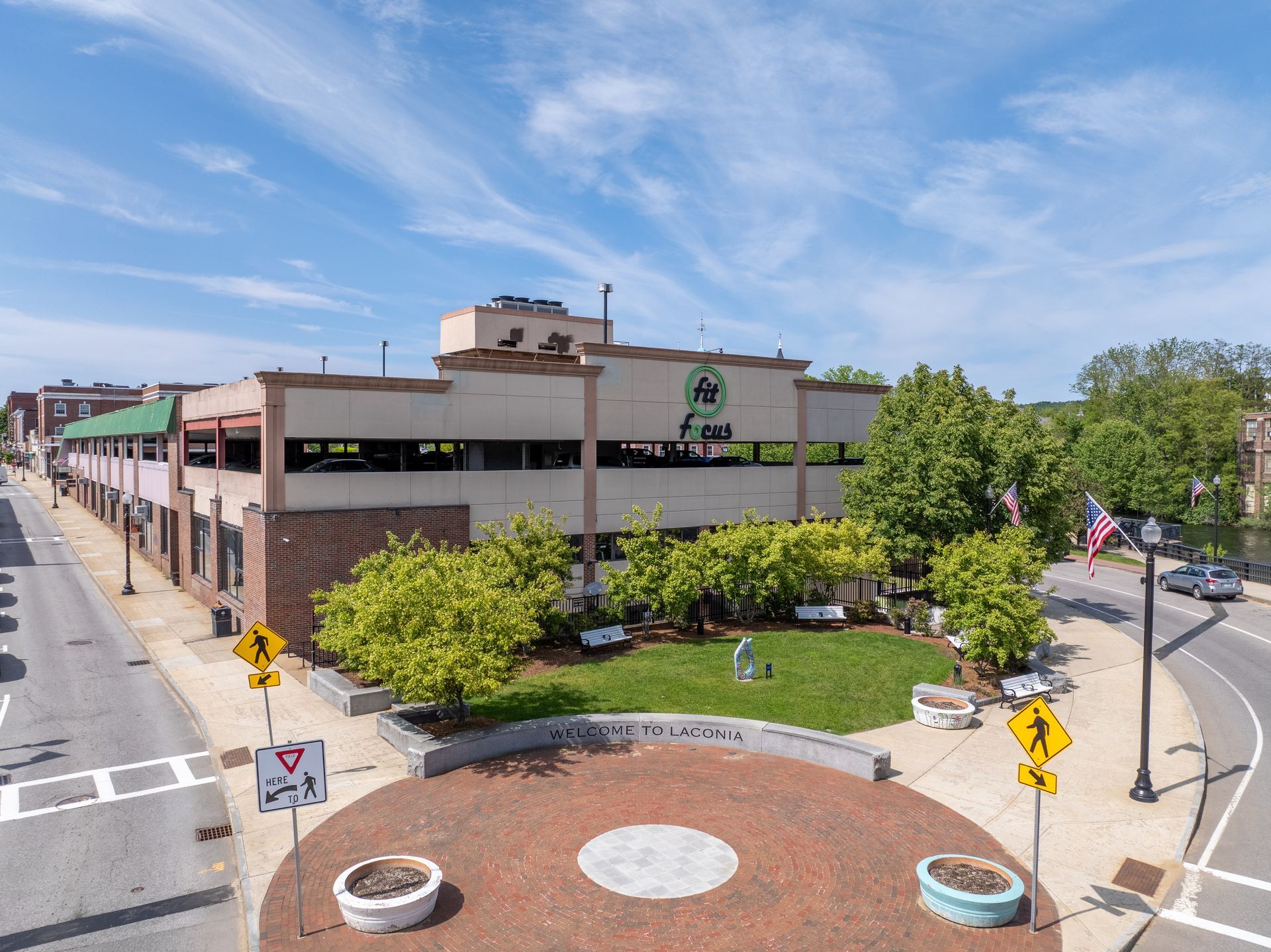 Exterior view of a two-story brick building, with a small circular park in front, under a blue sky.