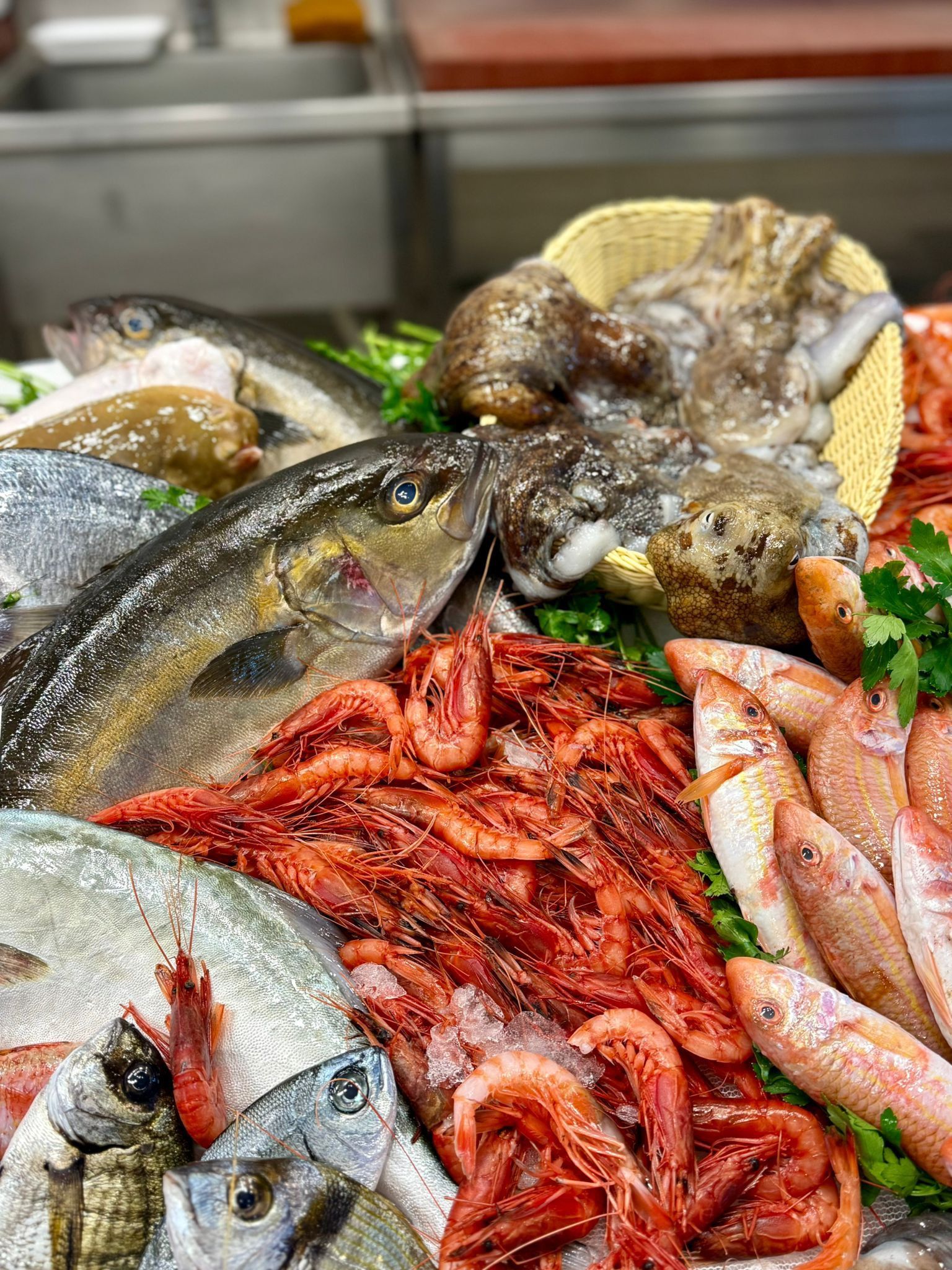 Esposizione di pesce fresco: pesce, polpo, gamberi e triglie su un bancone.