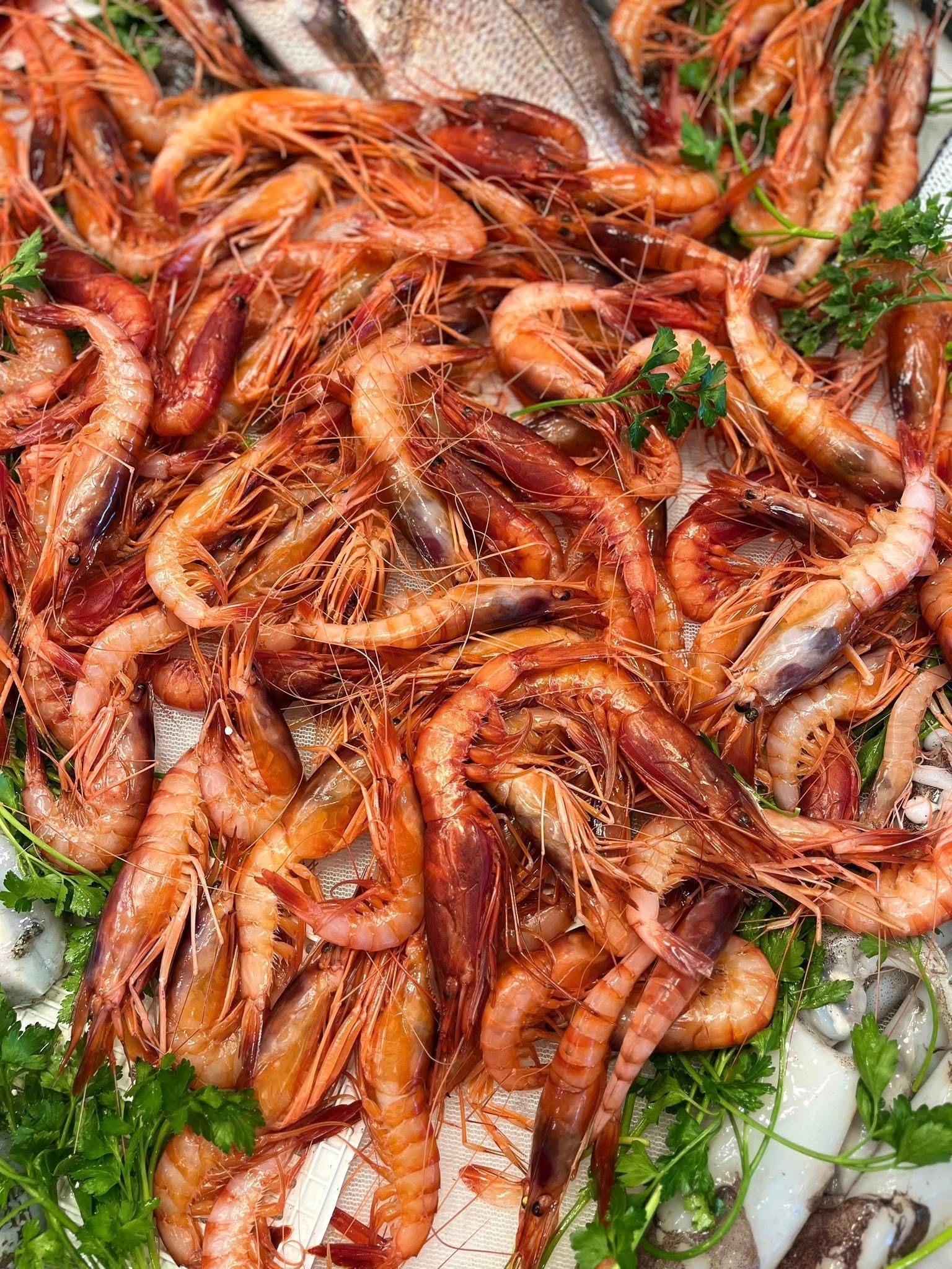 Mucchio di gamberi arancioni cotti su un letto di verdure, con qualche pezzo di calamaro bianco.