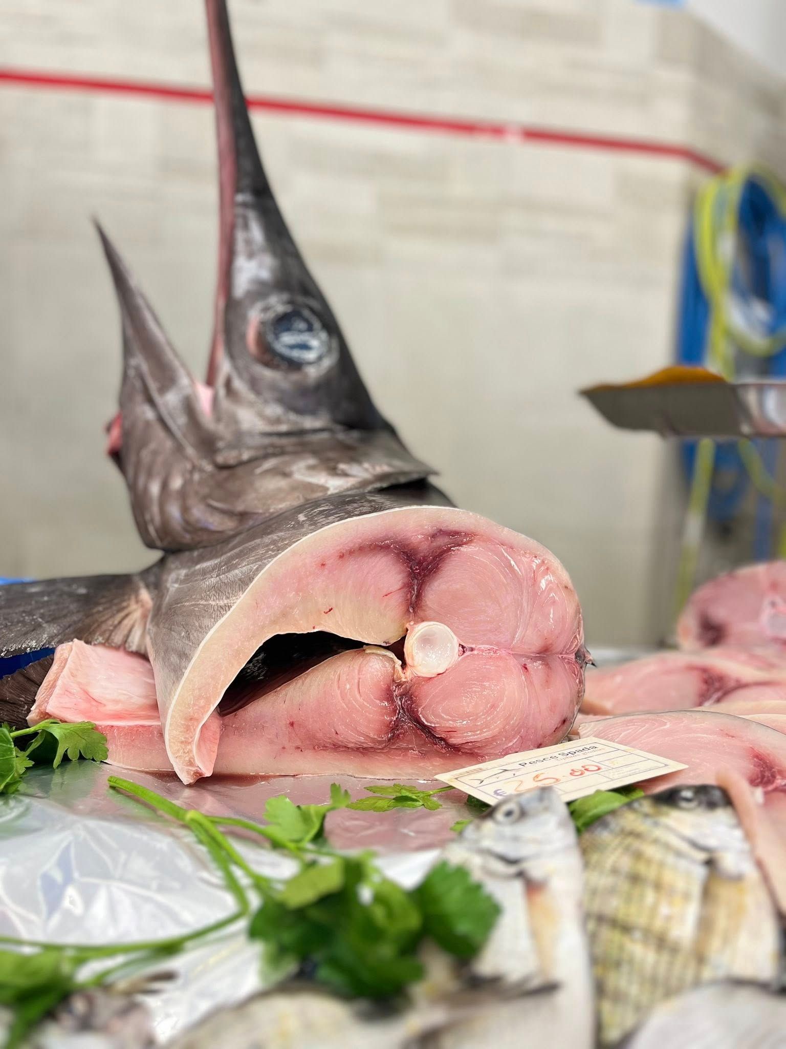 Pesce spada affettato al mercato del pesce, carne rosa pallido, con il lungo becco e la testa visibili dietro.