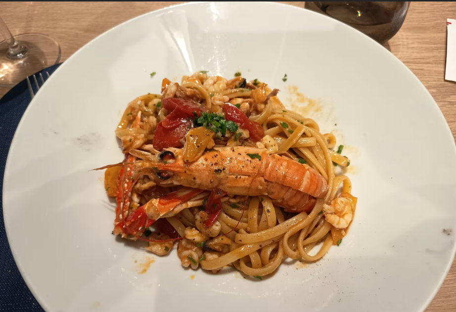 Piatto di pasta con gamberi grandi, pomodori e prezzemolo su un piatto bianco.