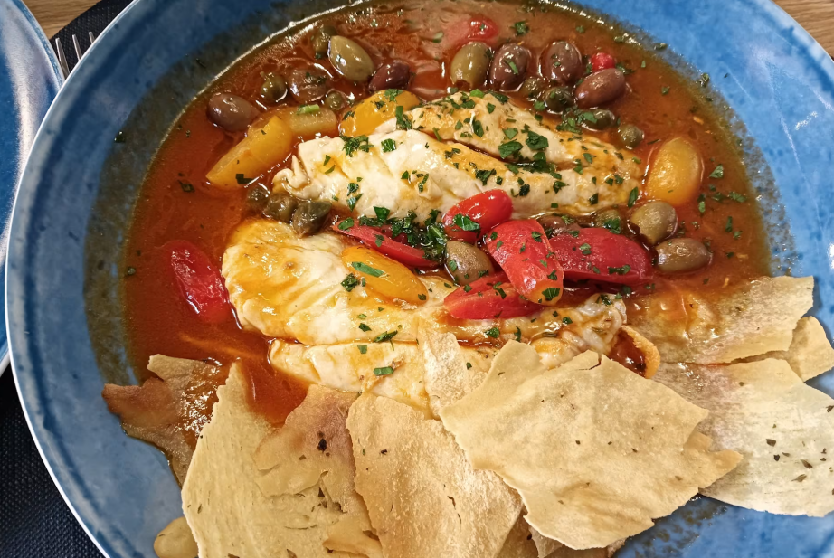 Piatto di pesce con salsa rossa, olive, peperoni, capperi e patatine croccanti in una ciotola blu.