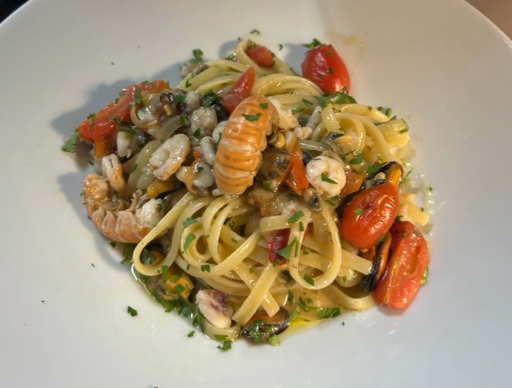 Linguine con frutti di mare, tra cui gamberi e pomodori, su un piatto bianco.