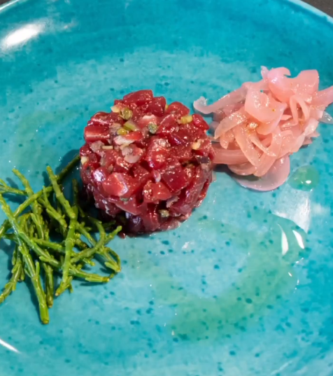 Tartare di tonno su un piatto verde acqua con zenzero sottaceto e rametti verdi.