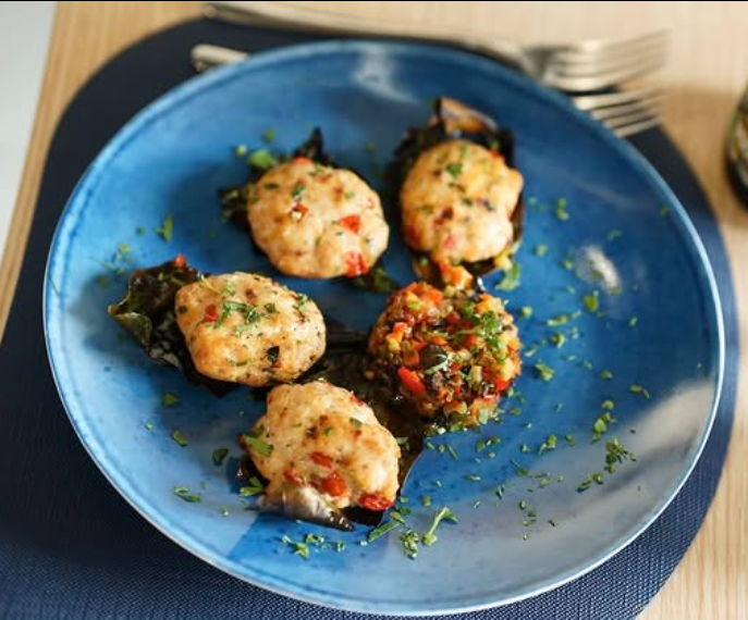 Cinque capesante ripiene su un piatto blu, guarnite con prezzemolo.