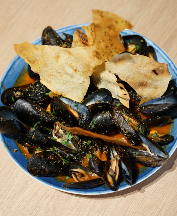 Ciotola di cozze in salsa, guarnita con cracker di pane piatto.