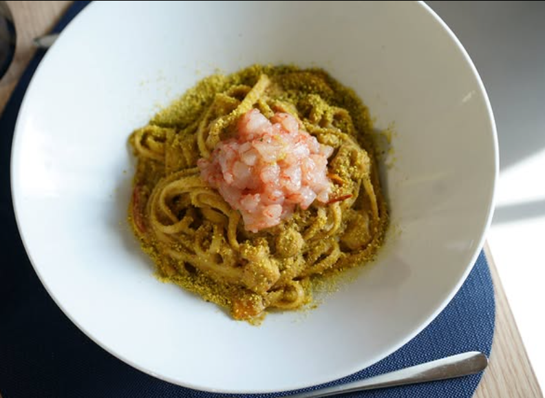 Pasta con salsa verde e gamberi in una ciotola bianca.